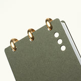 A close-up of the Discbound Analog + 3 Refills, a dark green brass disc-bound notebook with three small round holes on the cover, shown on a plain white background—a refined, refillable task planner.