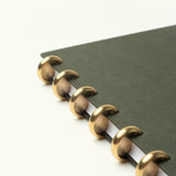 A close-up of the Discbound Journal Bundle (Standard 6"x 8.5" Journal + 3 Refills) featuring a refillable dark green cover and large gold-colored disc binding rings on a white background.