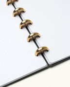 Elevate your note-taking with the Discbound Journal Bundle (8.5" x 11" Journal + 3 Refills), featuring elegantly bound dotted pages with brass discs. This open, refillable notebook—captured from above on a white background—is the perfect choice for everyday journaling and organization.