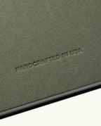 A close-up of a textured, olive-green surface with the words HANDCRAFTED IN USA embossed in uppercase letters. The lighting accentuates the rich texture and indentation of the text, reflecting the artisanal quality present in every Discbound Journal Bundle (8.5" x 11" Journal + 3 Refills)—including those featuring striking brass discs—all carefully crafted to be both refillable and distinctive.