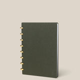 The Discbound Journal (Standard 6"x 8.5") features a dark green minimalist cover and gold-colored solid brass discs, shown standing upright on a plain beige background.