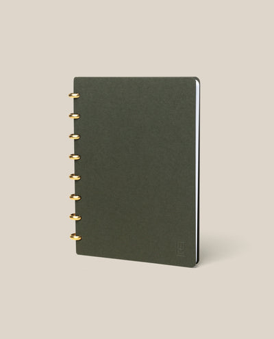 The Discbound Journal (Standard 6"x 8.5") features a dark green minimalist cover and gold-colored solid brass discs, shown standing upright on a plain beige background.
