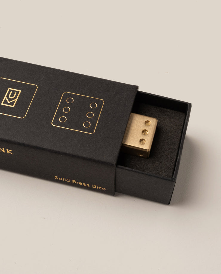 Gold dice in a black box with 'MANK' branding on a beige background