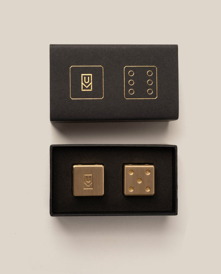 Gold dice set with black boxes on a beige background
