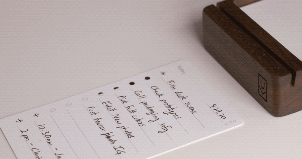 A handwritten to-do list on a notepad includes tasks like Film desk scene, Pick kit colors, and Edit new photos. The notepad rests near a wooden stand. The date 4.29.20 is written at the top right.