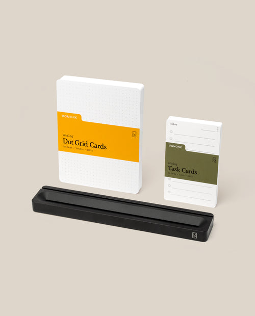 The Analog Card Bar - Essentials Kit (Black Aluminum), including Task Cards, Ugmonk Dot Grid Cards, and a sleek black card holder, is thoughtfully arranged on a neutral background to create an elegant desk organizer setup.