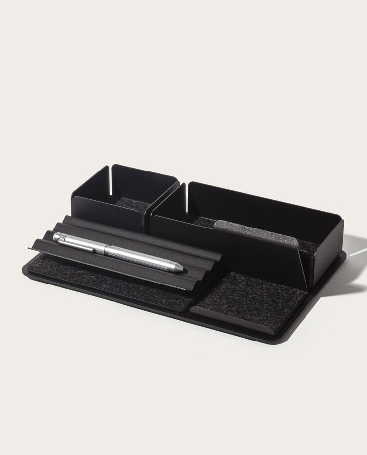 The Gather 2x3 Base Plate (Black) is a minimalist desk organizer made in Pennsylvania with two square compartments, a grooved section for a silver pen, and a felt pad on a rectangular base, shown against a plain white background.
