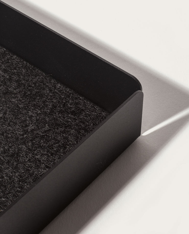 A close-up of the Gather Large Tray (2x2 - Black) featuring a textured dark felt interior and magnetic base, casting a shadow on a white surface in bright light.
