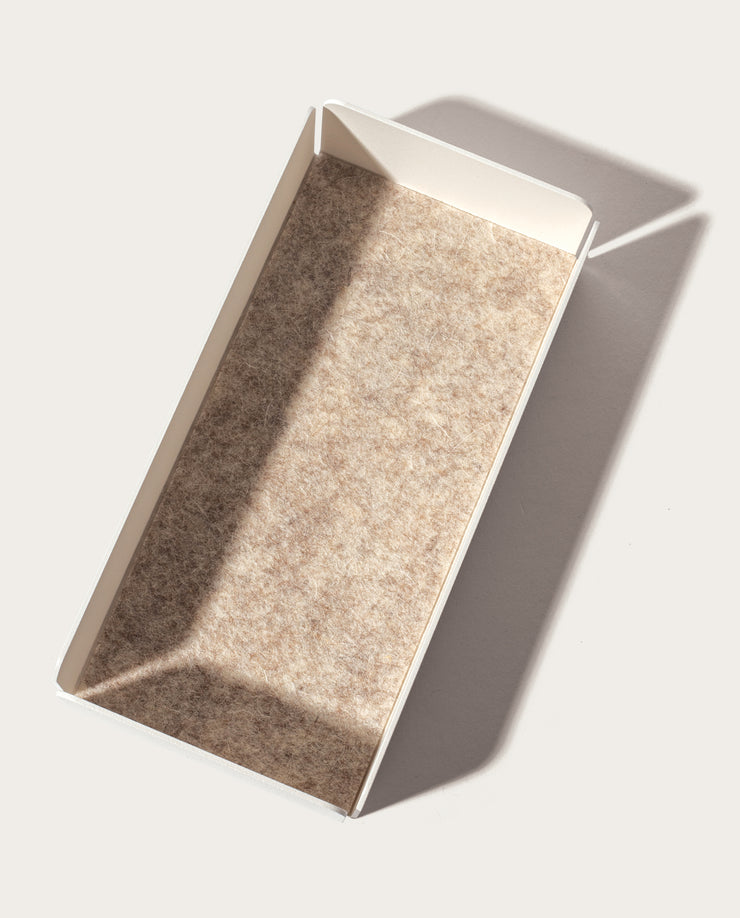 The Gather Medium Tray (2x1 - White) is a rectangular, shallow valet tray with a beige textured bottom, made of powder-coated steel. It sits empty on a light surface, angled in soft light from the upper left.