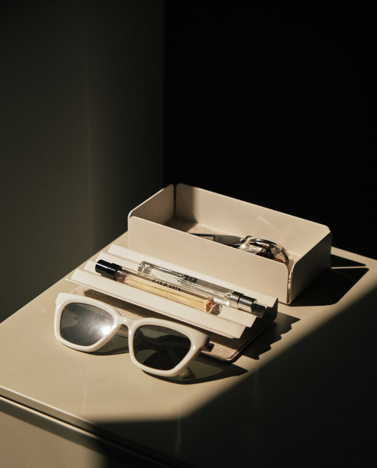 A pair of white sunglasses, a pen, and a small perfume bottle sit on the Gather Medium Tray (2x1 - White) next to an open cream-colored box, all highlighted by dramatic sunlight and shadows.