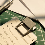 A close-up of a handwritten to-do list secured with HMM Clips (Set of 2 - Raw) to a notepad on a green cutting mat, with a pen and white paper sheets arranged neatly and sunlight illuminating the organized workspace.