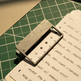 A stack of handwritten to-do lists—meetings, research, updates—is secured by HMM Clips (Set of 2 - Raw) on a green cutting mat as warm sunlight casts gentle shadows across the scene.