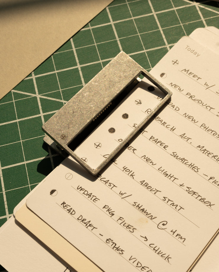 A stack of handwritten to-do lists—meetings, research, updates—is secured by HMM Clips (Set of 2 - Raw) on a green cutting mat as warm sunlight casts gentle shadows across the scene.