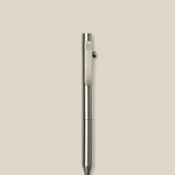The INVENTERY Bolt Action Pen (Stainless), a sleek stainless steel ballpoint with a clip, is displayed vertically against a plain light beige background.