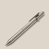 A sleek, metallic silver INVENTERY Bolt Action Pen (Stainless) with a clip and push-button mechanism is set diagonally from bottom left to top right, shown against a plain light beige background.