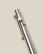 A close-up of the INVENTERY Bolt Action Pen (Stainless) with a clip, highlighting its sleek stainless steel design against a plain, light beige background.