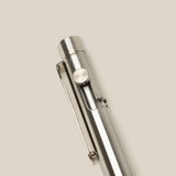 A close-up of the INVENTERY Bolt Action Pen (Stainless) with a clip, highlighting its sleek stainless steel design against a plain, light beige background.