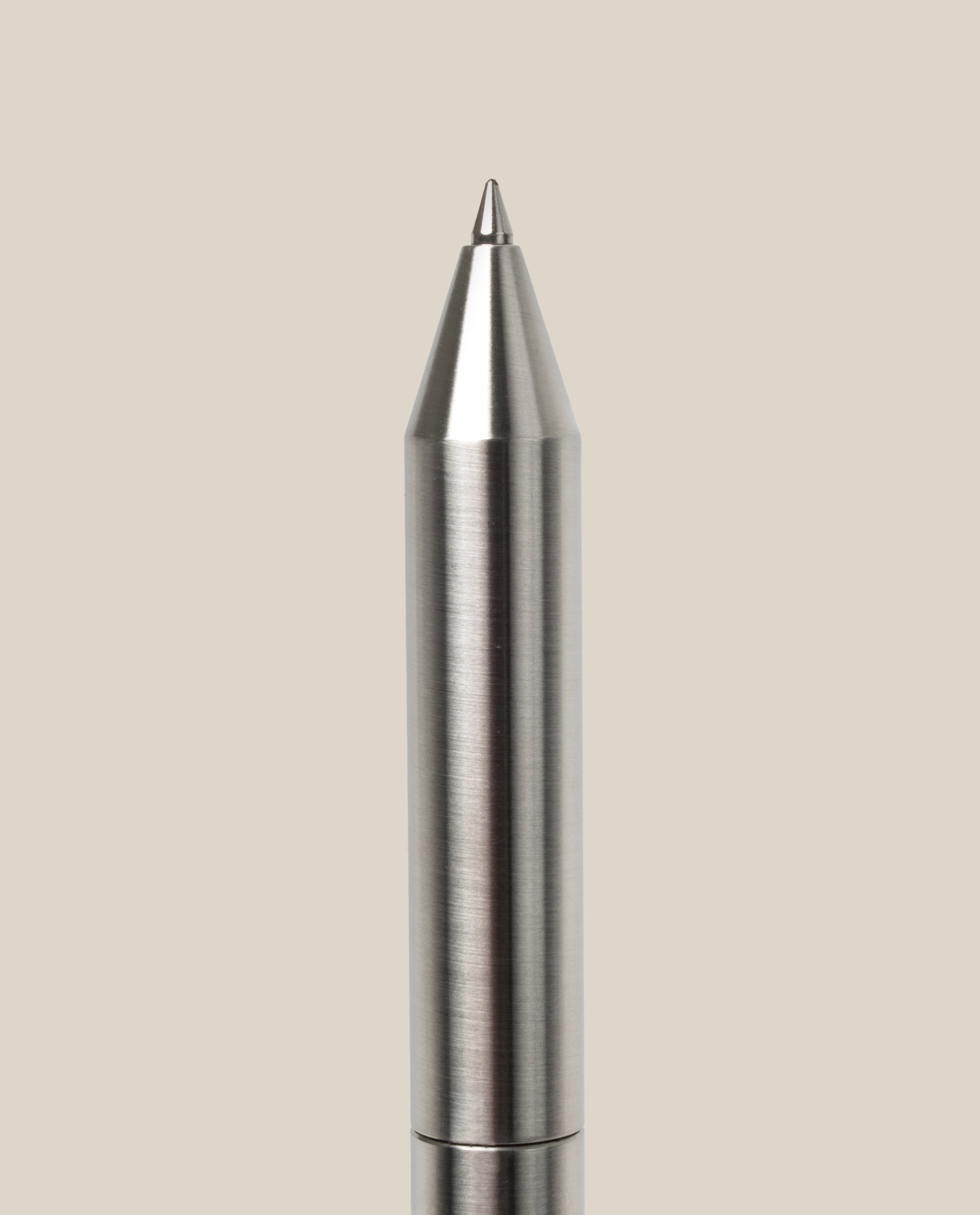 A close-up of the INVENTERY Bolt Action Pen (Stainless) with a brushed stainless steel finish, displayed vertically against a plain light beige background.
