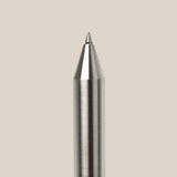 A close-up of the INVENTERY Bolt Action Pen (Stainless) with a brushed stainless steel finish, displayed vertically against a plain light beige background.