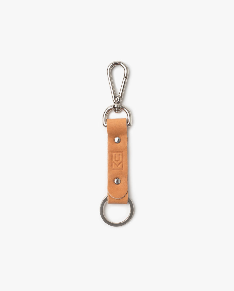 A tan leather keychain featuring a metal clip at one end and a key ring at the other, with two metal rivets and a small embossed logo on the leather strip.