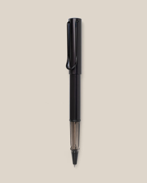 A black LAMY AL-star Rollerball pen with a transparent section near the tip is vertically centered on a plain beige background, highlighting its smooth writing experience and refillable rollerball design.