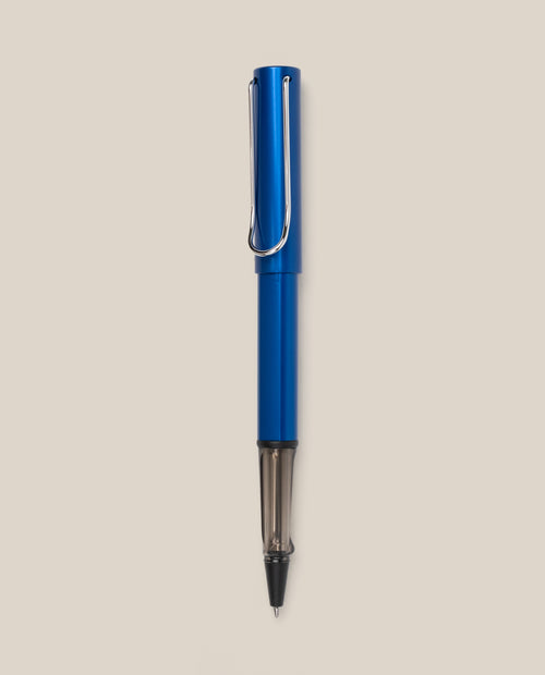 A LAMY AL-star Rollerball (Oceanblue) with a metal clip stands vertically on a light beige background, featuring smooth writing and a stylish design.
