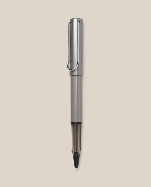 A graphite LAMY AL-star Rollerball with a sleek design stands vertically against a light beige background, highlighting its smooth writing performance and stylish, refillable rollerball pen construction.