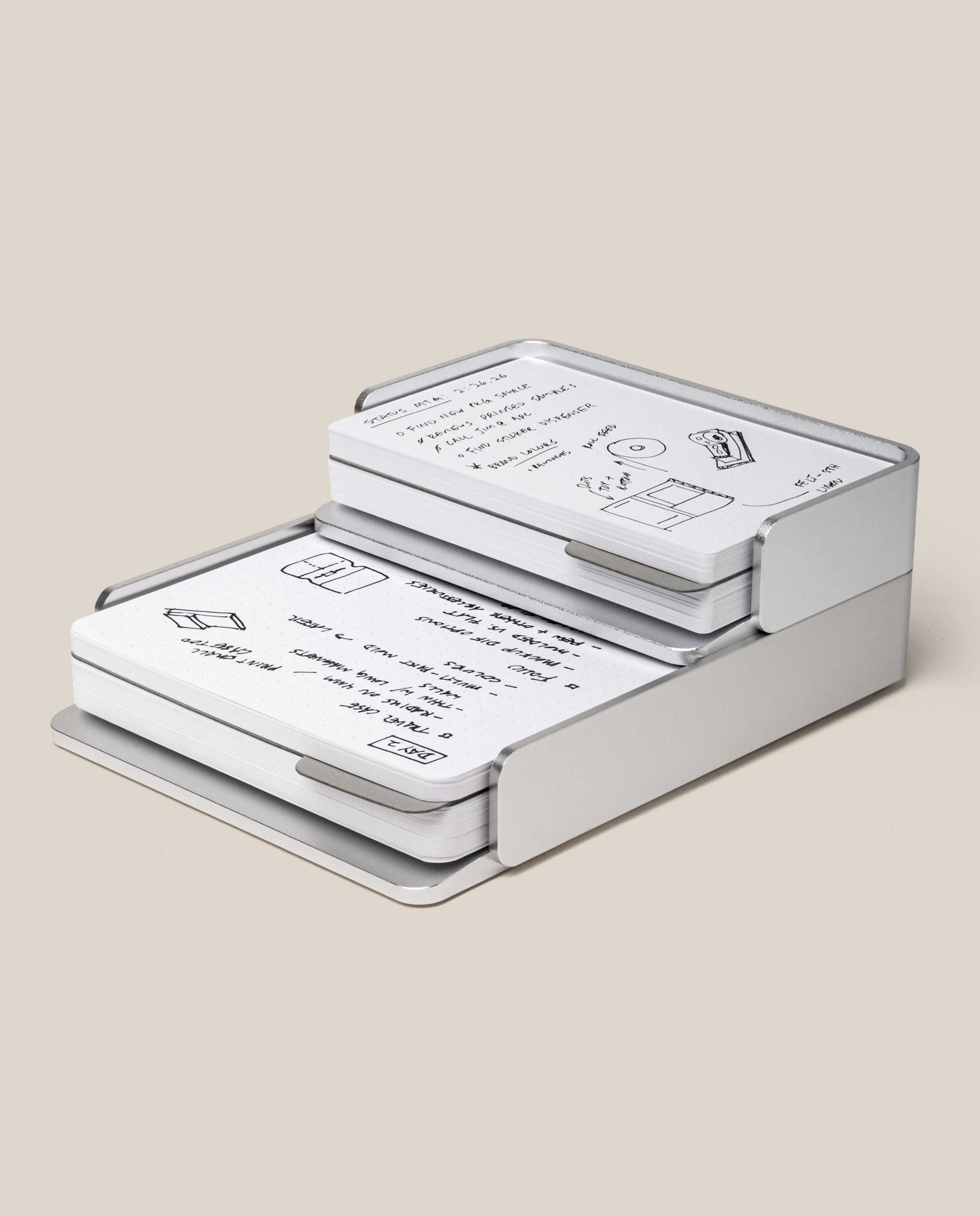 The Analog Capture Kit - Small & Large (Silver Aluminum) is a two-tier desk organizer for dot grid cards with hand-drawn black writing and sketches, shown on a plain beige background.