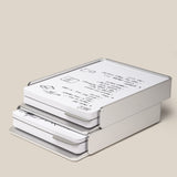 A stack of Analog Capture Kit - 2 Large (Silver Aluminum) trays holds neatly arranged paper with diagrams and text on a light beige background, showcasing a minimalist, modern design and an elegant silver aluminum card tray.