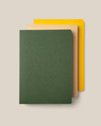 A set of three Layflat Notebook Bundle (Set of 3) notebooks are stacked on a beige background, featuring a dark green notebook with an embossed geometric pattern on top, a tan notebook in the middle, and a yellow notebook on the bottom. Each has rounded corners and durable Smyth sewn bindings that allow for effortless writing across every page.