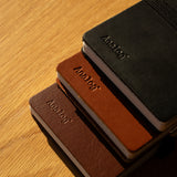 A Leather Discbound Analog + 3 Refills (Tan) notebook with a full-grain leather cover rests on a wooden surface, sunlight casting soft shadows across the scene.