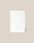 A Discbound Journal Refill - Lined (Standard 6″ x 8.5″) page, featuring a clean white surface with ruled lines and punched holes on the left, is centered against a plain beige background—ideal for adding to your Heirloom Discbound Journal.