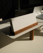 A Magnet Kit—featuring the Pen Tray and Analog Weekly—rests on a modern white desk, its minimalist paper calendar with blank weekly sections displayed in a wooden holder and the sleek Pen Tray neatly beside it, all illuminated by sunlight.