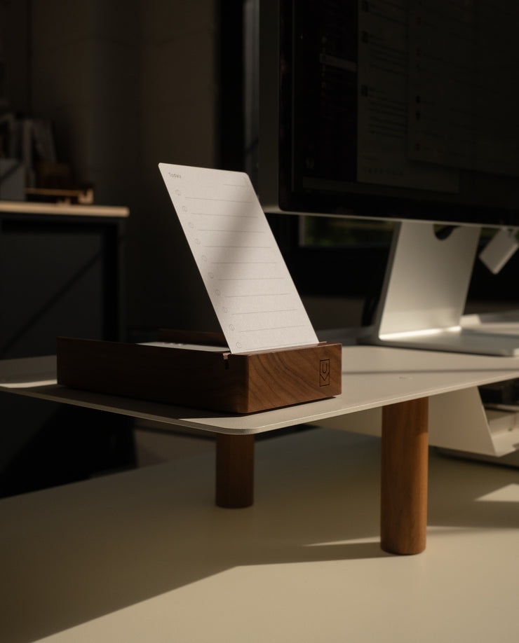 A Magnet Kit (For Analog Card Holder) secures the wooden holder with lined notepad to a white desk beside a monitor in a softly lit office, using strong adhesive magnets for neat, easy access.