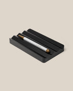 A silver and gold pen with "UGMONK" engraved rests in the Analog Multi Pen Tray (Black Aluminum) on a light beige background.
