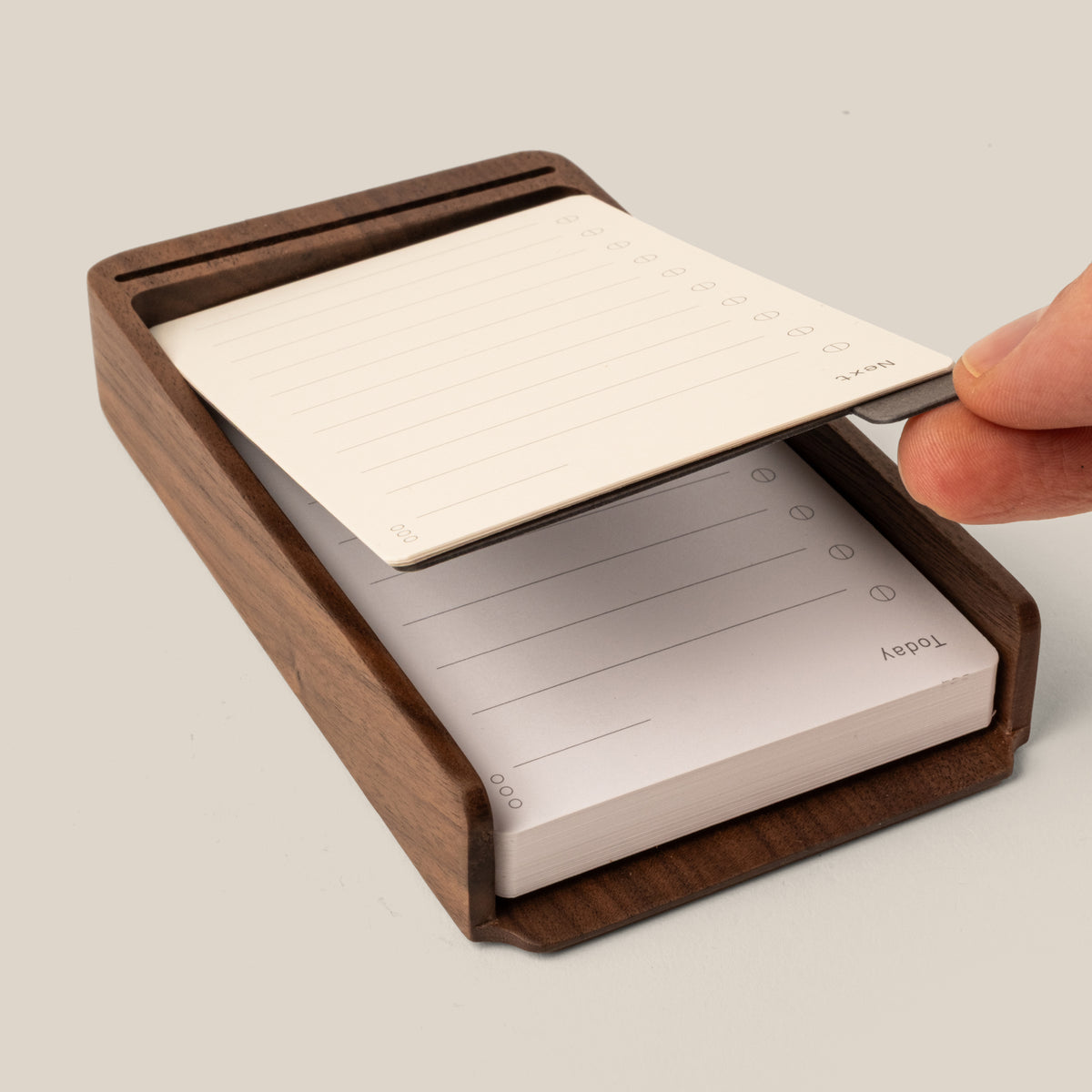 A hand lifts a lined notepad sheet from the Analog Annual Kit (Walnut), a wooden desk organizer designed as a Daily and Weekly Card Holder with checkboxes and lines for notes or tasks.