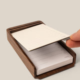 A hand lifts a lined notepad sheet from the Analog Annual Kit (Walnut), a wooden desk organizer designed as a Daily and Weekly Card Holder with checkboxes and lines for notes or tasks.