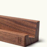 A close-up of the Analog Weekly Card Holder (Walnut), a handcrafted geometric stand with a small stylized U and V logo on its side, made in Pennsylvania.