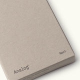 A minimalist, light brown cardboard box labeled "Analog" and "Next" in small black letters on the corners, designed for Analog - Next Cards (1-Pack). Ideal for organizing dot grid cards or goal-setting tools.