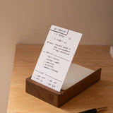 An Analog Dot Grid Card from the Small (3-Pack) sits upright in a wooden holder on a light desk, featuring handwritten notes for ad creative and video production—ideal for organized note taking. A black and gold pen rests nearby.