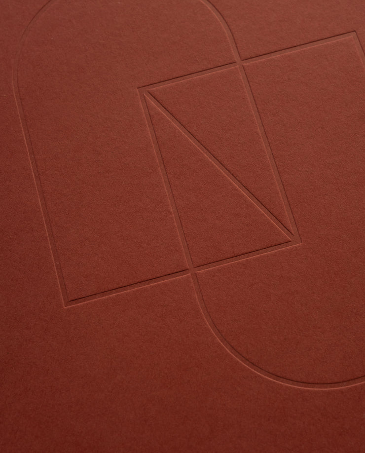 Embossed geometric shapes—a rectangle, triangle, and two semicircles—are outlined on the textured cover of the maroon Layflat Notebook.