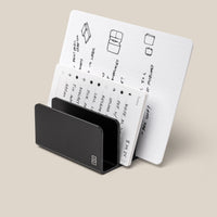 The Analog Card Organizer (Black Aluminum) displays multiple white cards with handwritten notes, diagrams, and sketches arranged in rows against a plain beige background.