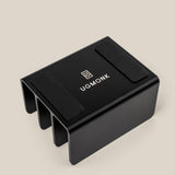 The Complete Analog Collection (Black Aluminum): a black, rectangular metal desktop organizer with three slots, two anti-slip pads on top, and a white UGMONK logo, shown against a light beige background.