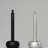 Two HMM Paperweight Pen Stands (Black), with hexagonal handles and round bases, are displayed side by side on a plain gray background, offering a quirky desk accessory that doubles as a pen stand or paperweight.