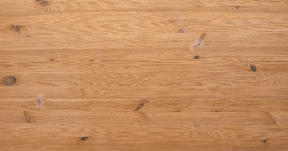 Close-up of a light-colored wooden surface with visible grain patterns, knots, and subtle imperfections, giving it a natural, rustic appearance.