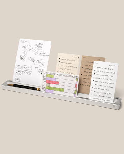 The Analog Card Bar (Large 16" – Silver) is a slim solid aluminum desk organizer that holds a pen and several task cards with handwritten notes, sketches, and lists, all neatly arranged against a beige background.