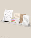 The Analog Card Bar (Large 16" – Silver) is a minimalist solid aluminum desk organizer that holds several task cards featuring sketches, lists, and charts, as well as a black pen and gold pencil. *Cards sold separately.