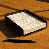 A black pen lies on a wooden table beside an open notebook filled with sketches, notes, and Analog Dot Grid Cards - Large (1-Pack). Sunlight casts soft shadows. Text in the corner reads: *Capture Tray sold separately.