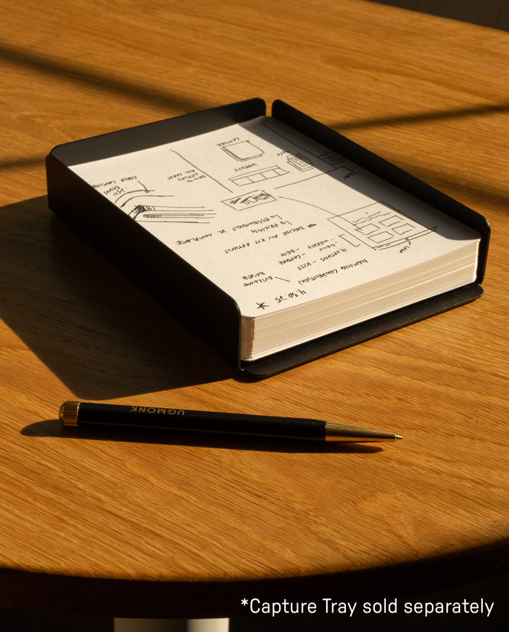 A black pen lies on a wooden table beside an open notebook filled with sketches, notes, and Analog Dot Grid Cards - Large (1-Pack). Sunlight casts soft shadows. Text in the corner reads: *Capture Tray sold separately.