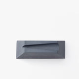 A rectangular, dark gray cast concrete Craighill Desk Knife Plinth (Slate) with a sloped, angular groove on top is shown as a sleek holder, set against a plain white background.